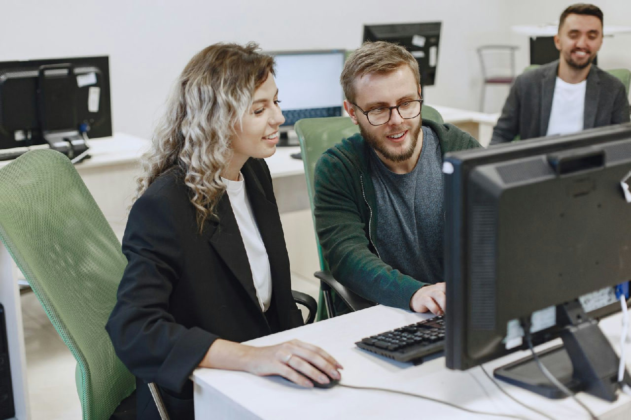 Duas pessoas trabalhando juntas em um computador em um escritório, acompanhando o processo comercial.